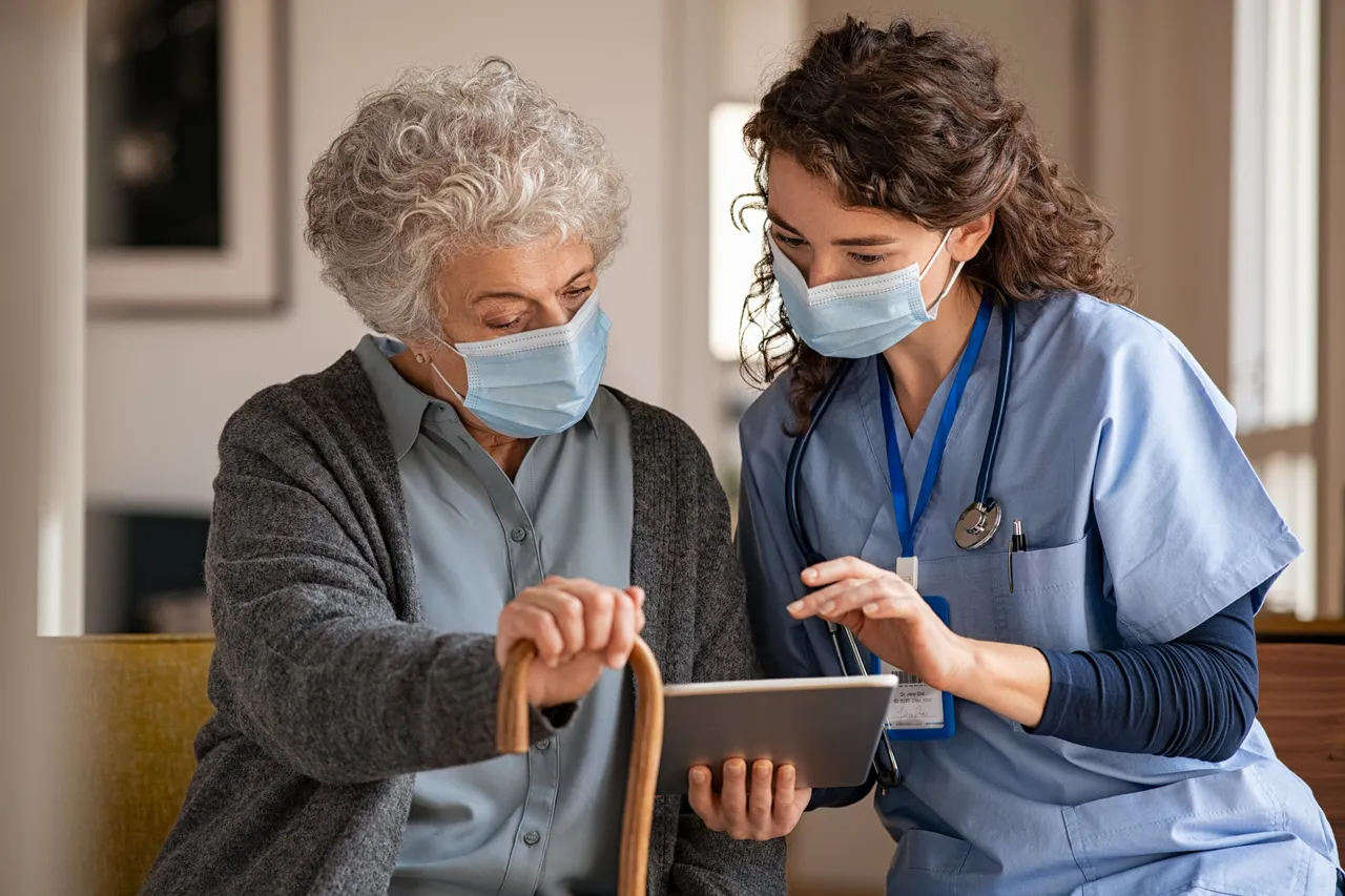 Caregiver using a digital tablet with an older adult during a senior care visit